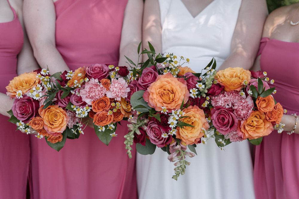 Wedding party members hold vibrant orange and pink bouquets against pink dresses at an elegant celebration.