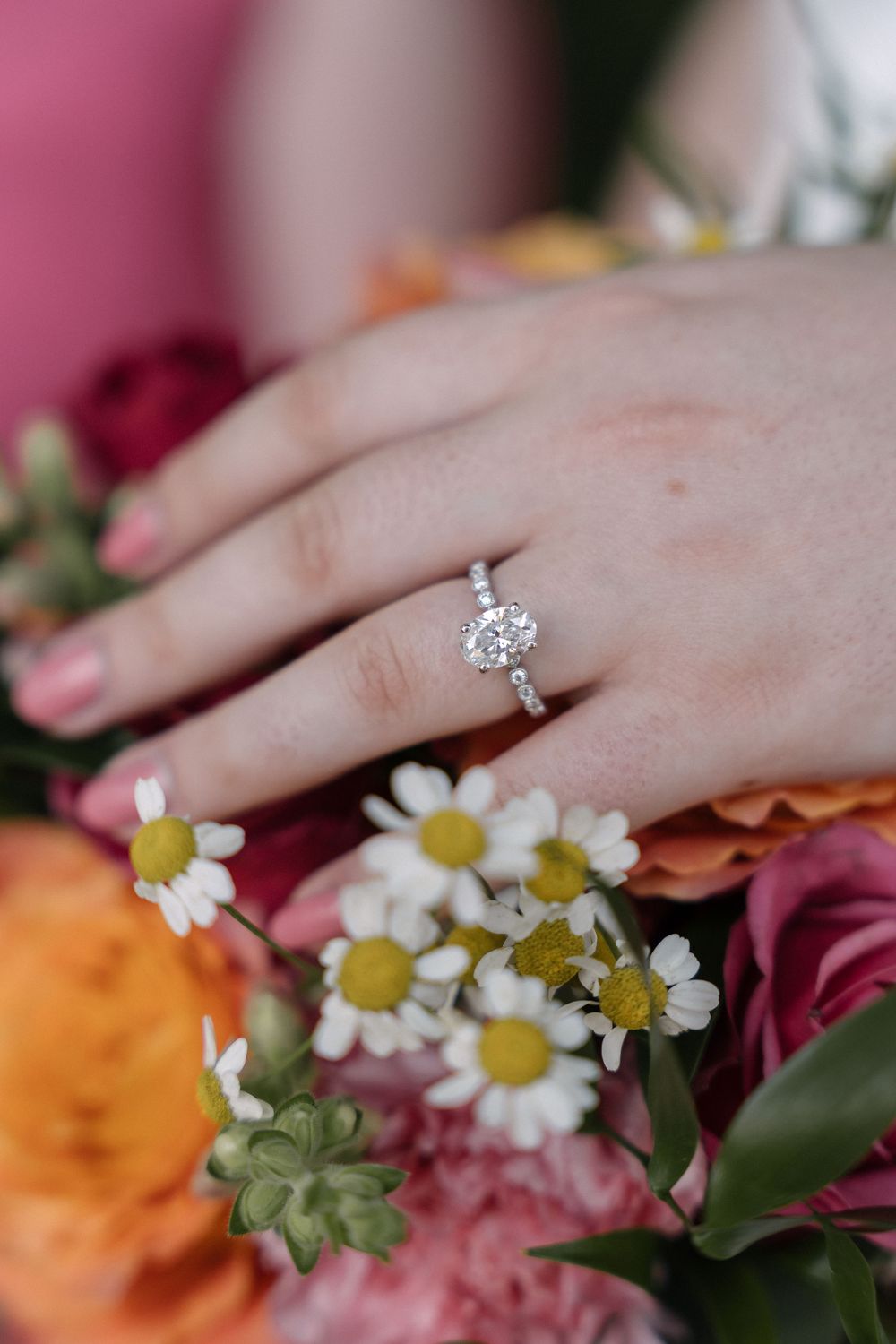 Close up shots of an engagement ring with diamond solitaire surrounded by delicate daisies and pink flowers.