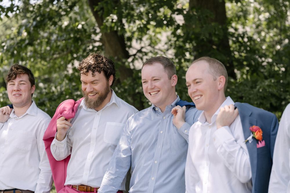 A group of men in dress shirts smile together outdoors with floral boutonnieres during a spring celebration.