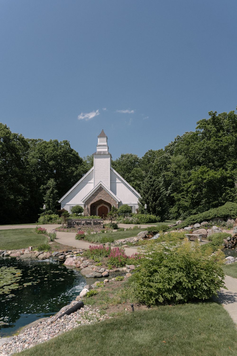 White church chapel set on a landscaped hillside with stone retaining walls and vibrant gardens in summer.