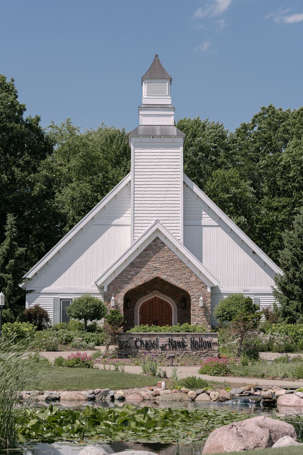 Stone and white chapel with multiple spires nestled among lush greenery and decorative rock gardens.