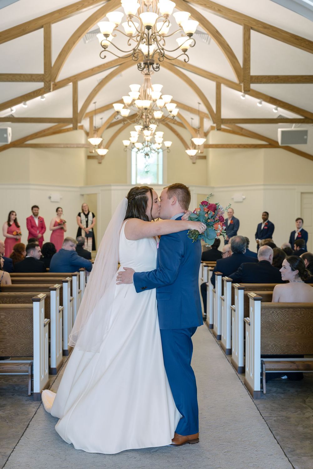 A couple shares their first dance in a chapel with exposed wooden beams and elegant chandeliers overhead.