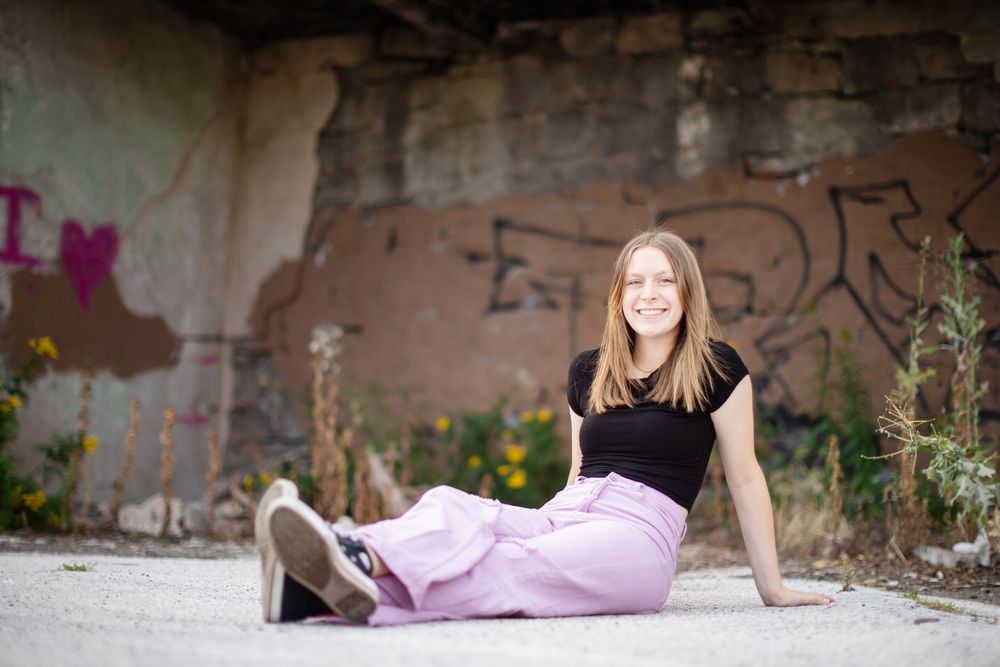 Woman in pink dress poses casually near brick wall with spray paint art.