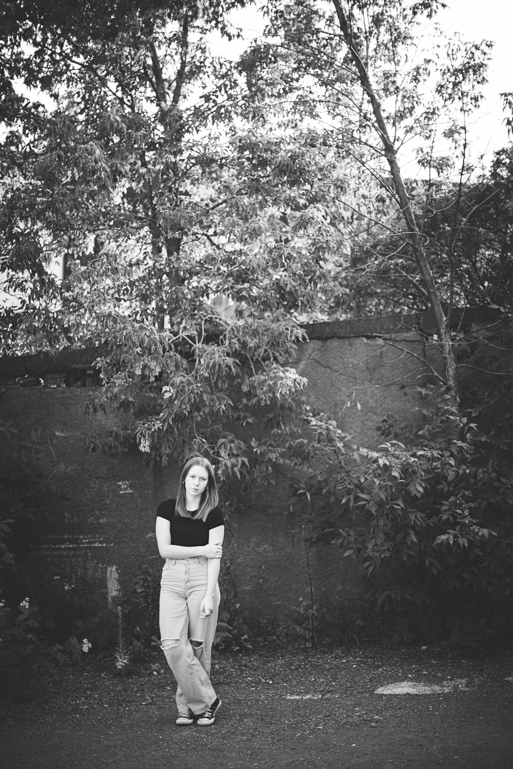Black and white artistic photo showing a person in casual attire standing near trees in a natural outdoor setting.