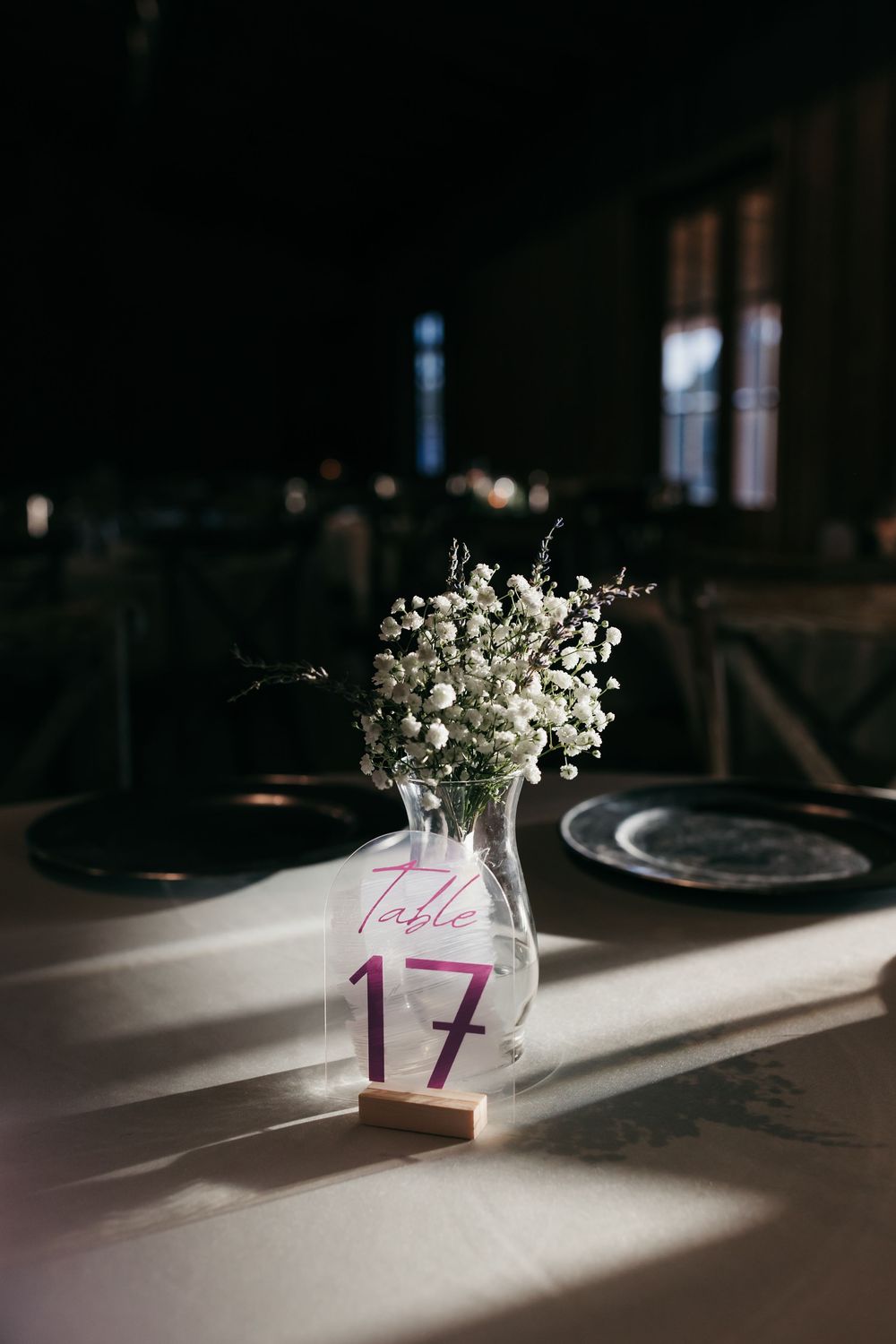 White flowers in glass vases cast dramatic shadows across a dark wooden table in low-key lighting.