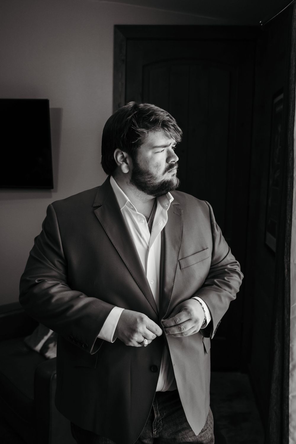 Black and white portrait of a person in a business suit adjusting their jacket while looking away from the camera.