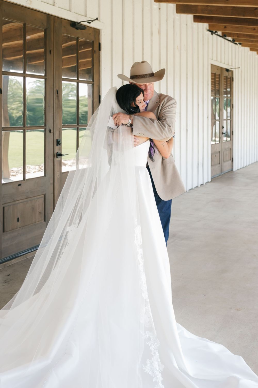 A couple embraces on their wedding day on a rustic porch, with the bride wearing a flowing white gown and long veil.