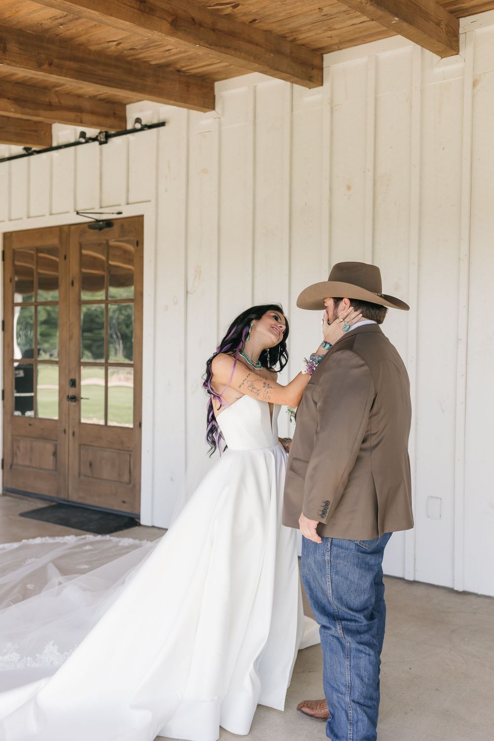 A couple shares a tender moment on their wedding day under a rustic wooden beam ceiling at a country venue.