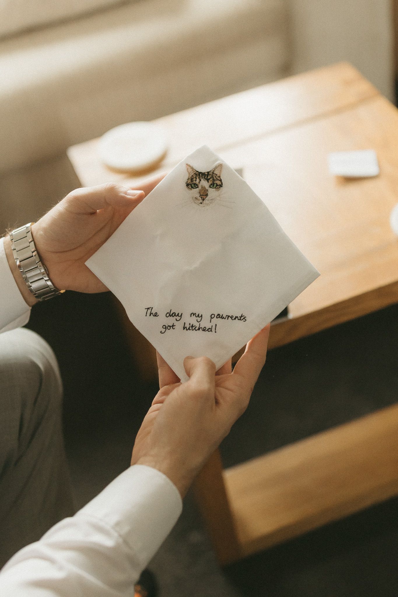 A hand in a white sleeve holding and opening a white paper letter on a wooden table in warm lighting.