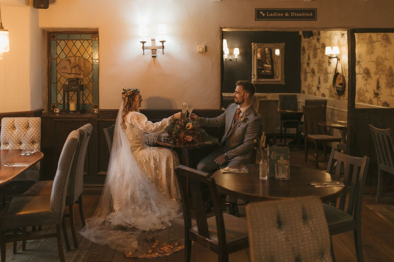Wedding party seated at elegant wooden dining tables in a rustic restaurant setting with warm lighting.