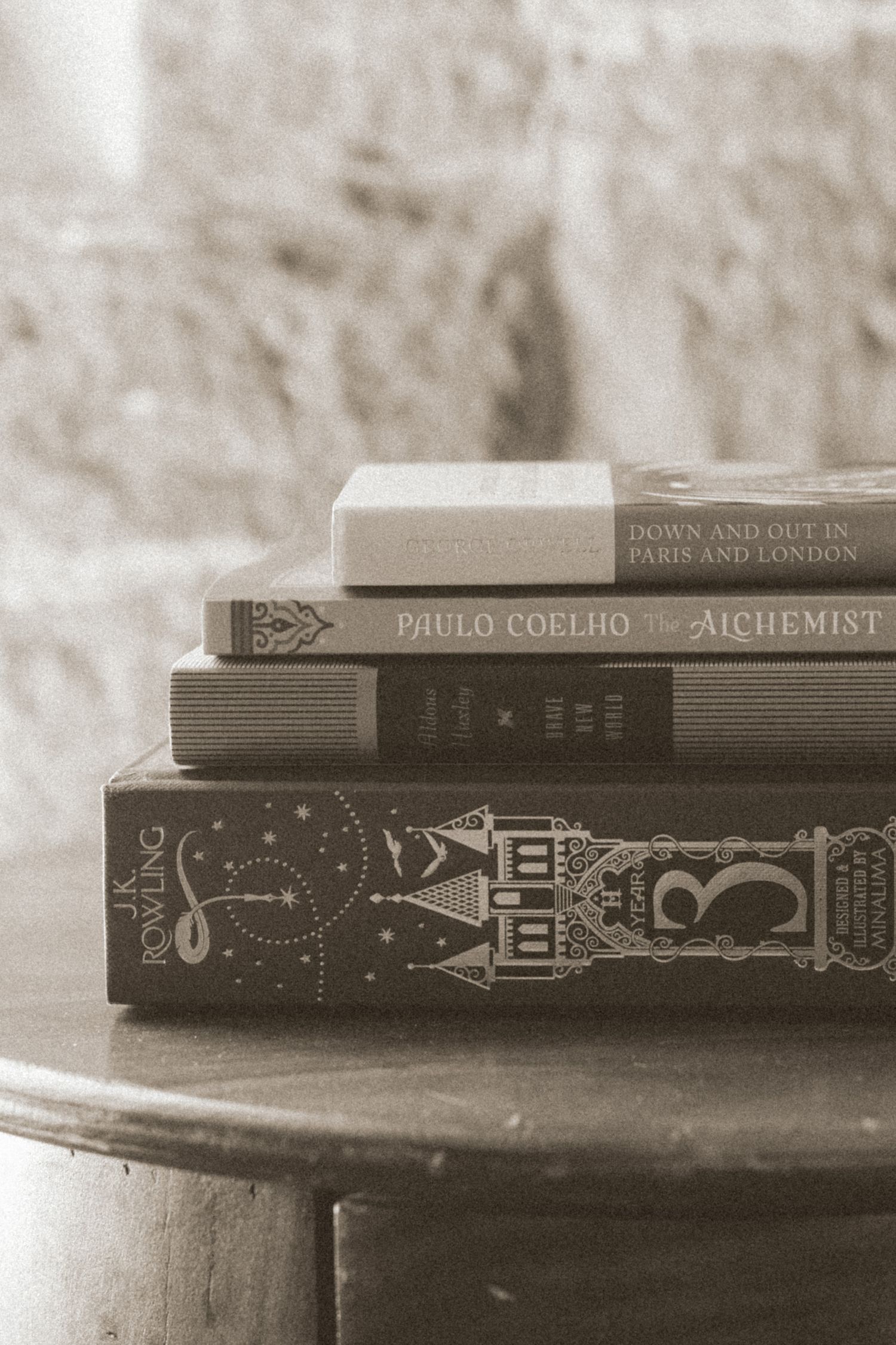 Stack of books including Paulo Coelho's The Alchemist in antique-style sepia photography.