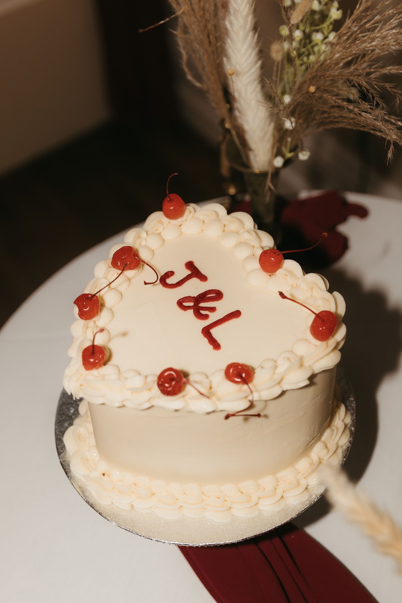 White heart-shaped wedding cake decorated with tiny red cherries and delicate piping on a white tablecloth.