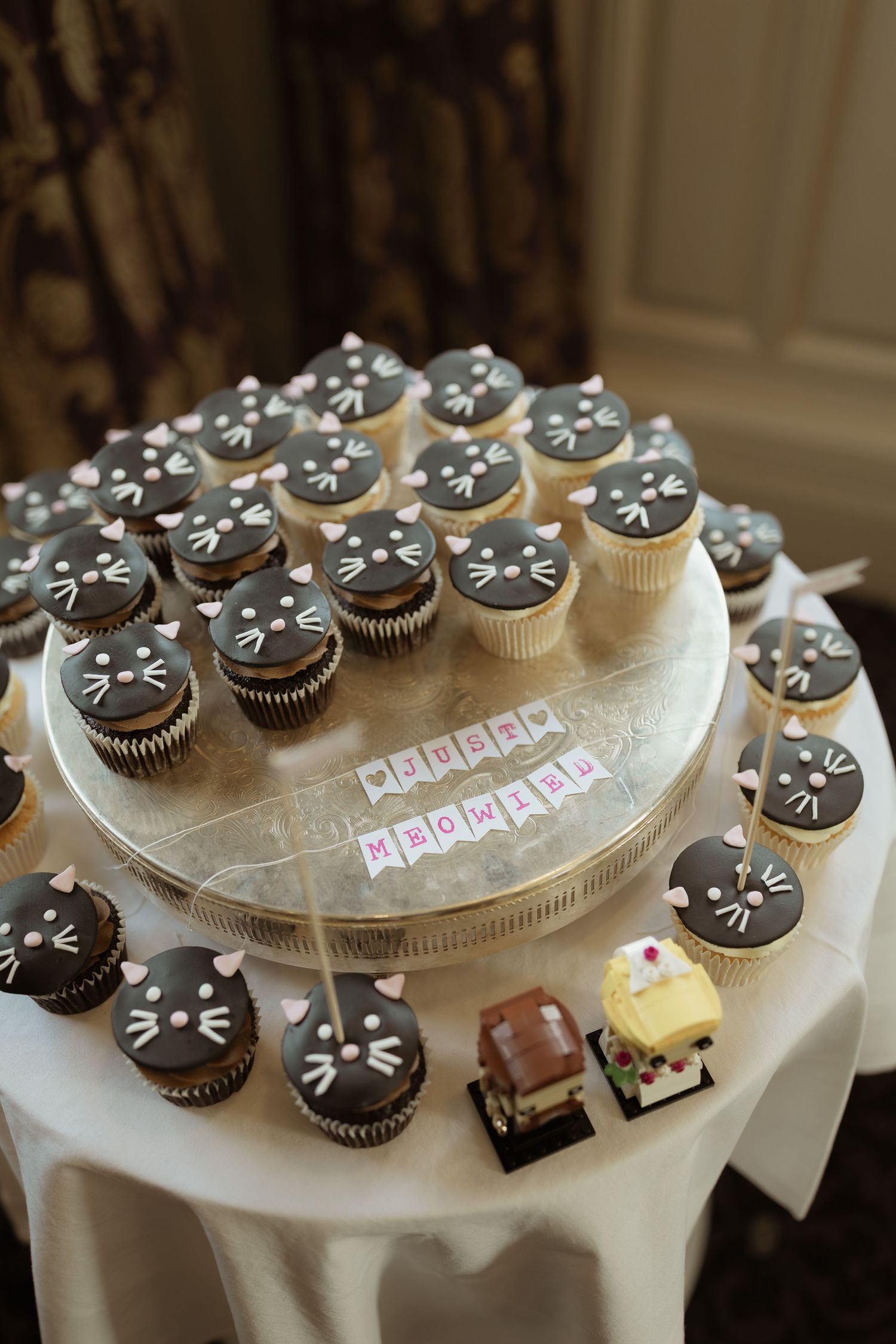 Chocolate cupcakes decorated like black cats arranged on a white cake stand for a special occasion celebration.
