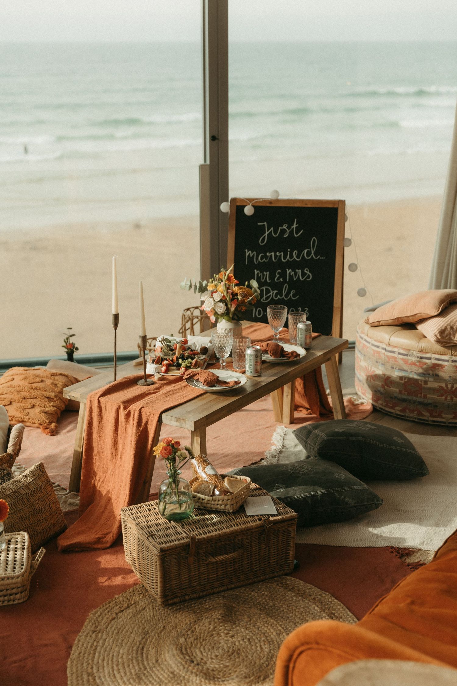 Aesthetic beachside dining setup with terracotta linens, woven decor, and rustic chalkboard signs against an ocean backdrop.