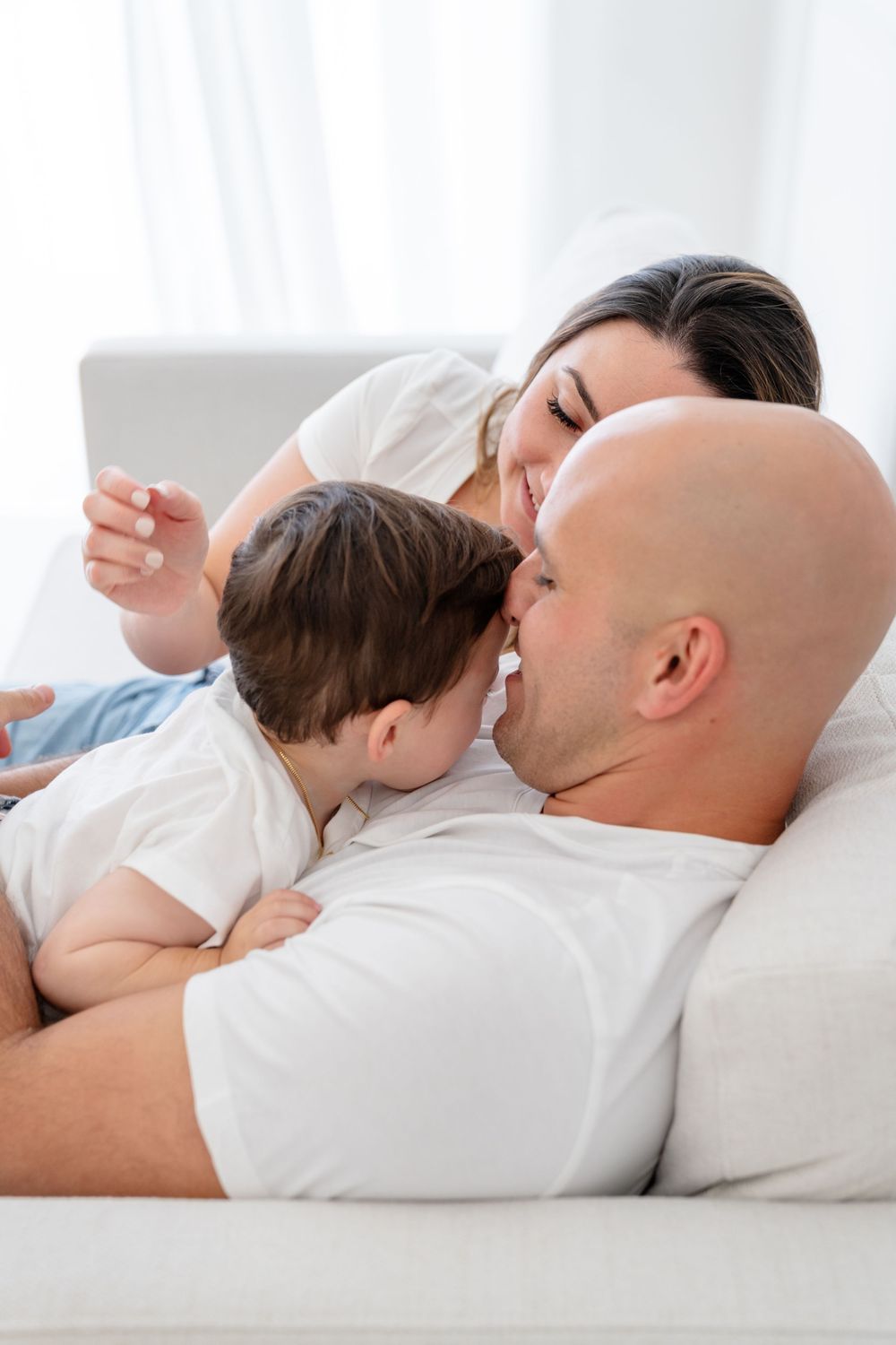 Family resting together on white couch wearing matching white shirts in tender moment at home.