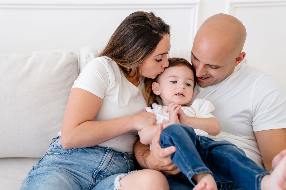 A cozy family moment of three people in casual attire snuggling together on a white couch.