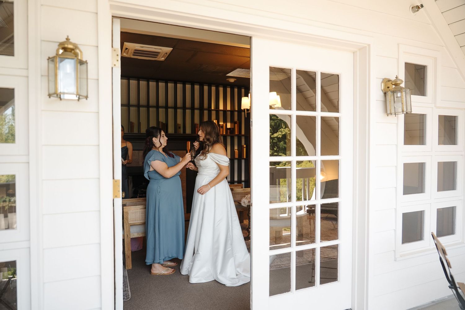 Wedding guests mingle and wait by white French doors and windows of an elegant traditional venue entrance.