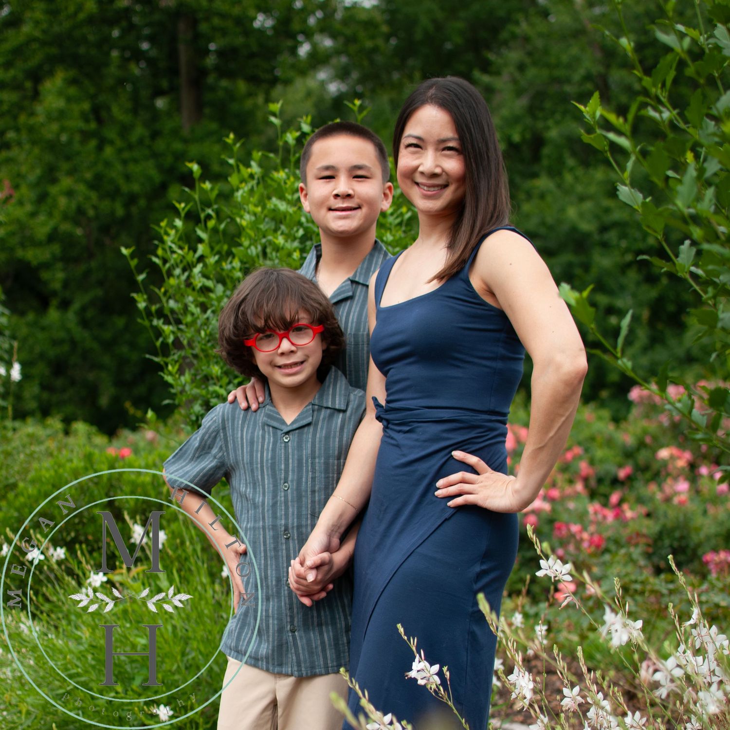 A family poses together in a blooming garden with pink and white flowers while wearing blue and striped outfits.