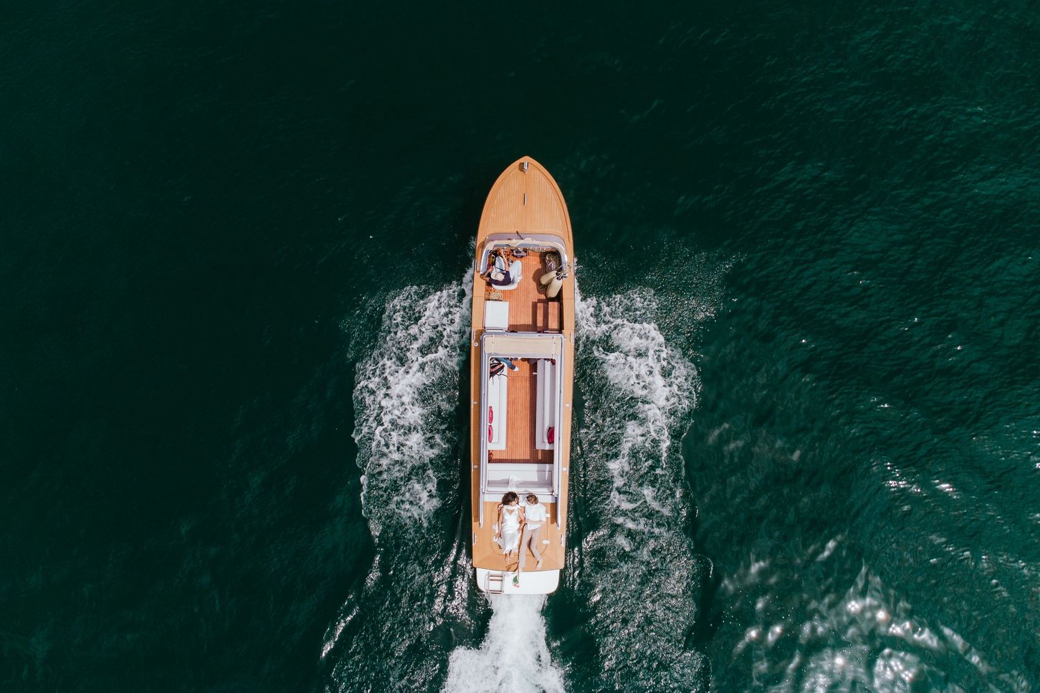 Aerial view of a yacht sailing through turquoise tropical waters with a white wake trailing behind.