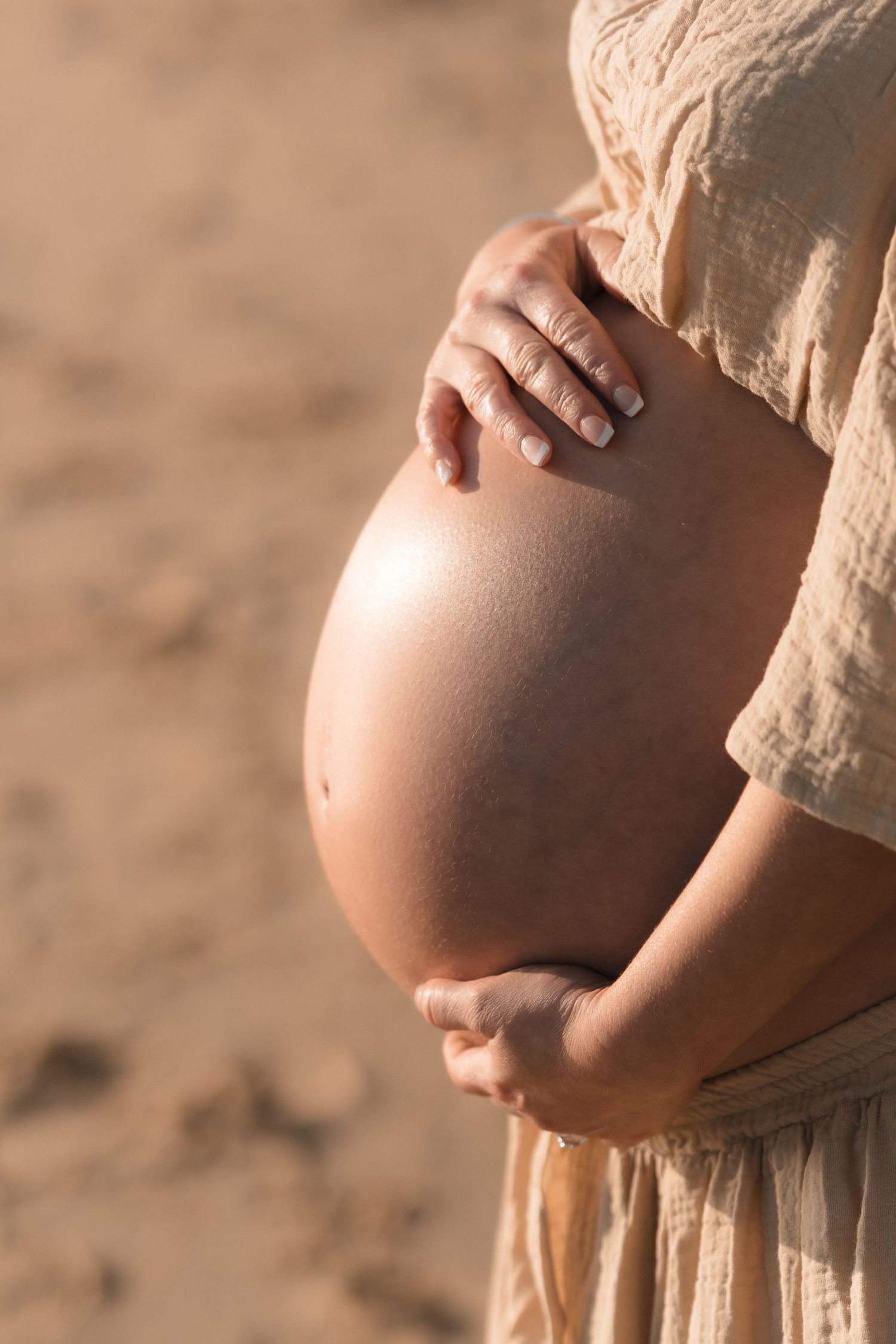 Series of close-up photos showing pregnant person's growing belly in beige dress against neutral background.