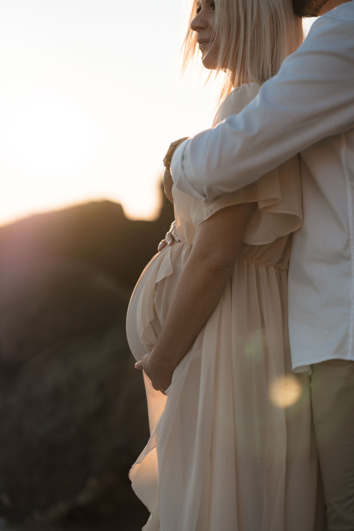 Side view of an intimate maternity photo with a person in a flowy beige dress during golden hour sunset.