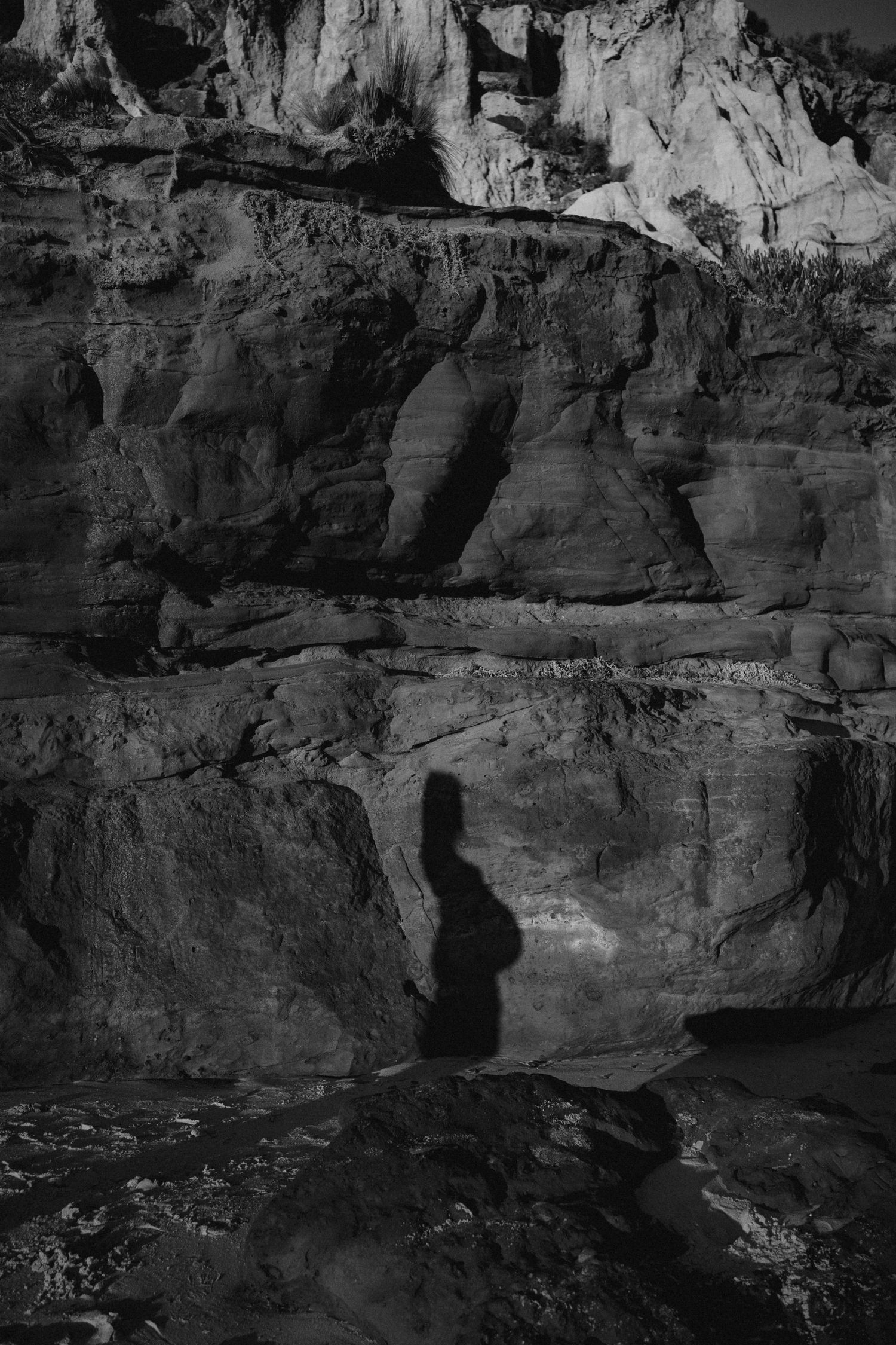 Rocky cliffs and caverns cast dramatic shadows in black and white monochromatic landscape photography.