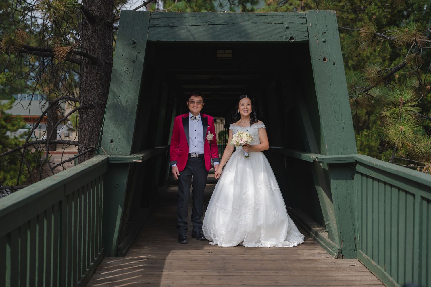 People walking through a covered wooden bridge at a wedding against a backdrop of trees.