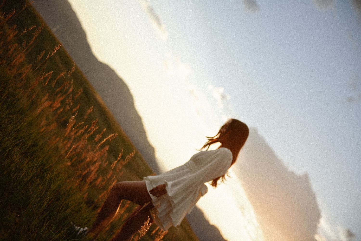Silhouette of person in white dress standing in field at sunset with dramatic angled perspective.