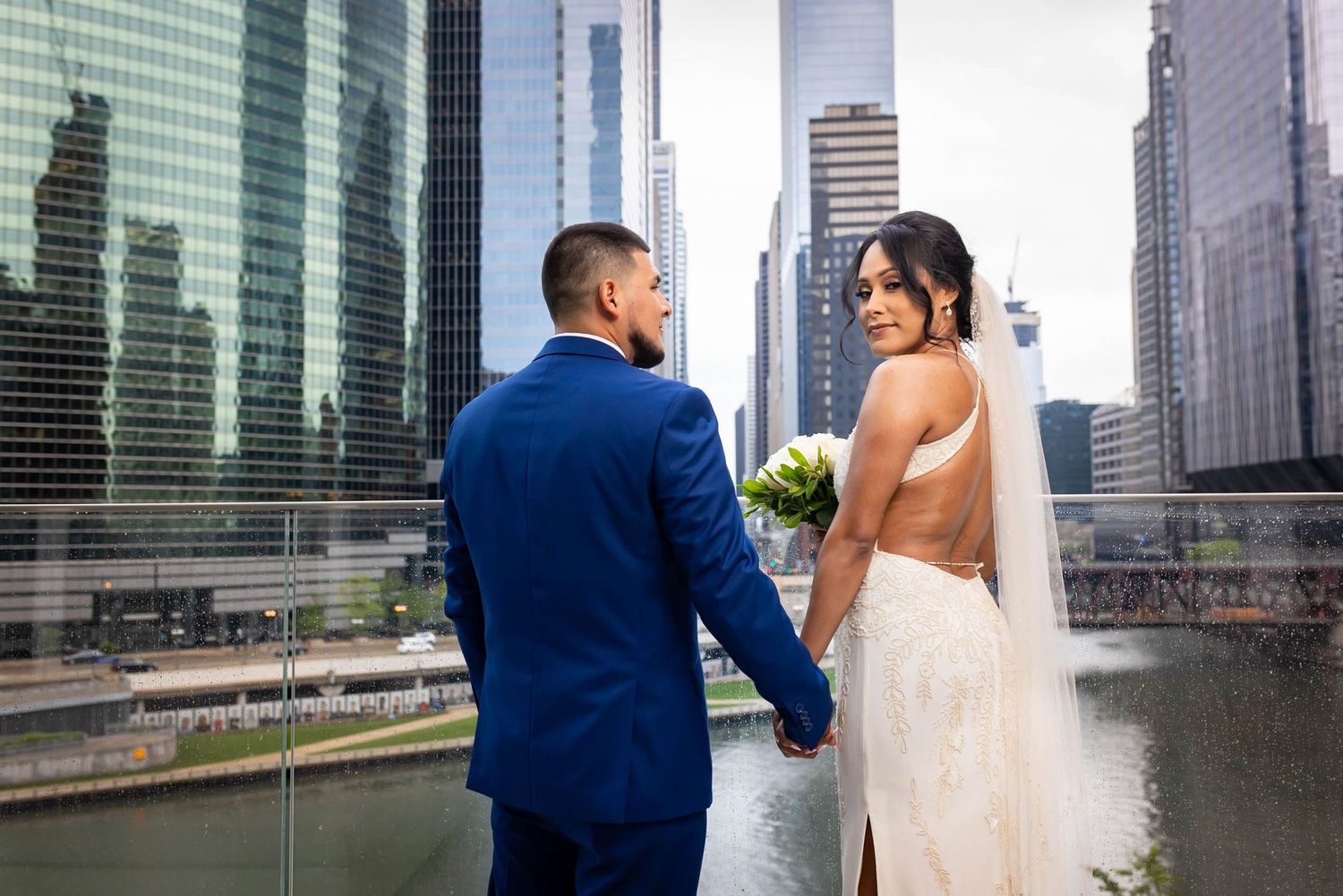 A bride and groom share a moment along the Chicago River with skyscrapers in the background.