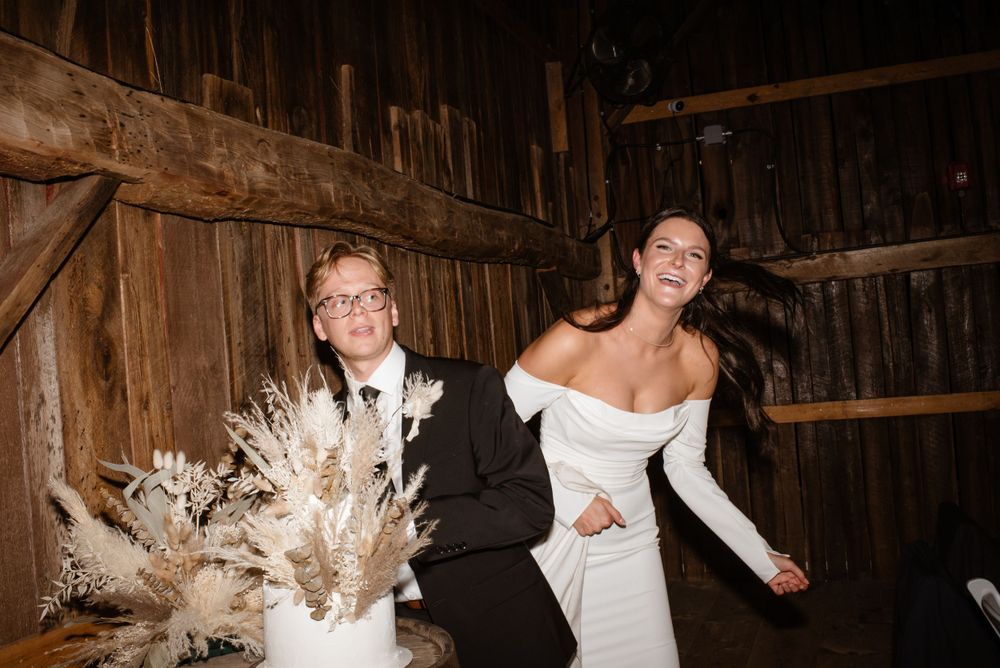 A couple shares a joyful moment dancing together in a rustic wooden barn with pampas grass decor.