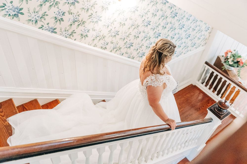 Person in a wedding dress walking up a vintage wooden staircase with white spindles and wooden handrail.