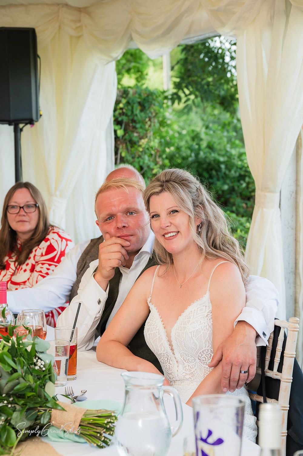 The wedding reception speeches are under way in a white marquee, with guests seated at decorated tables during an outdoor celebration.