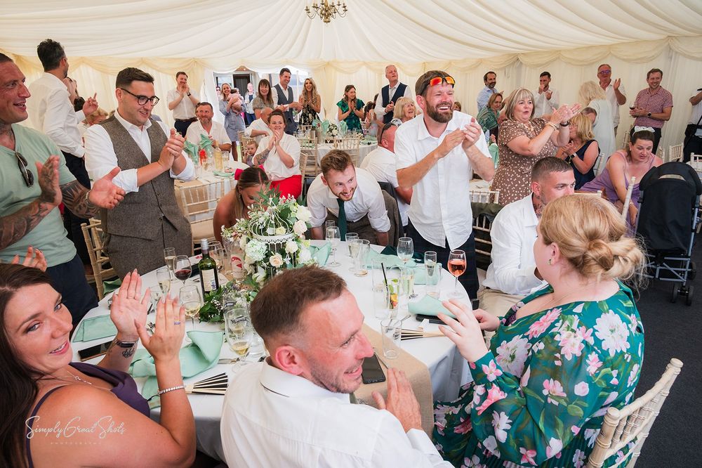 Wedding reception guests at decorated tables in a white marquee celebrate during dinner and festivities.
