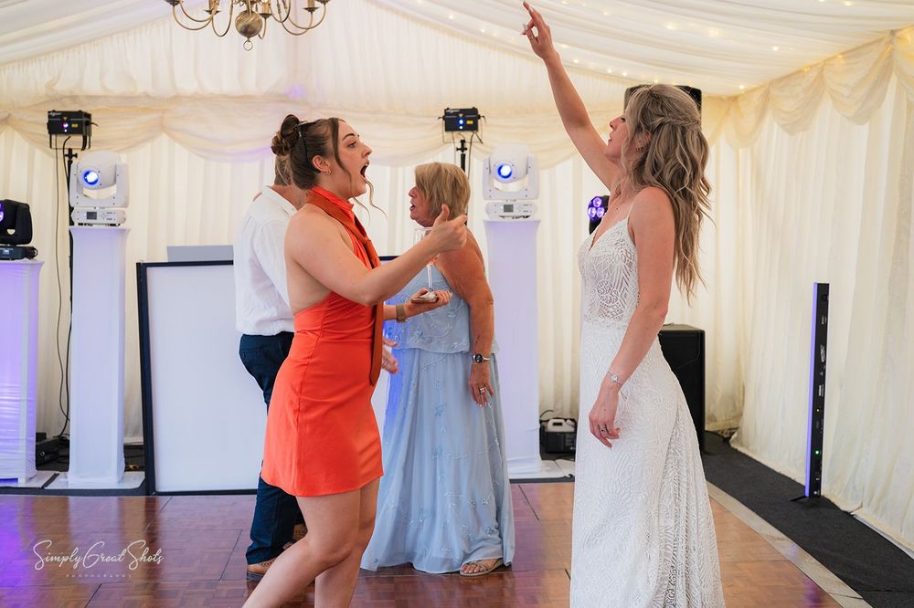 People dancing and celebrating at a wedding reception in a white marquee with purple accent lighting.