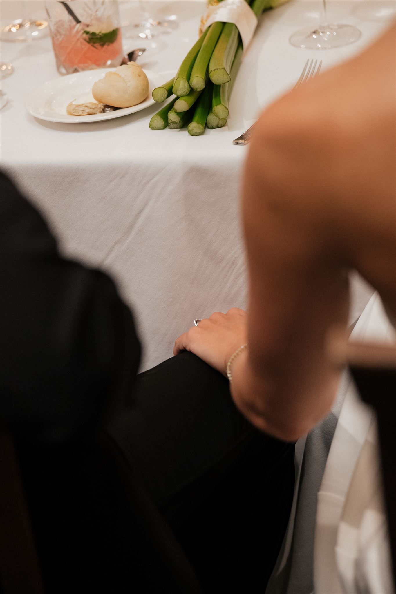 A table setting at a formal dinner with white linen, asparagus, and wine glasses visible in the background.