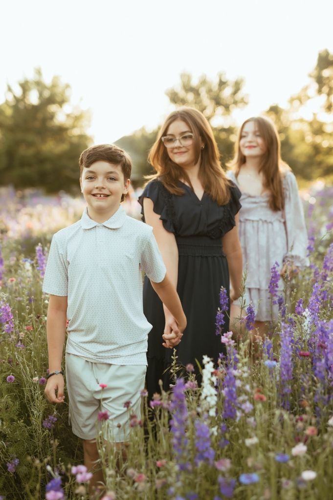 Family stands together in a field of purple wildflowers during golden hour sunset.