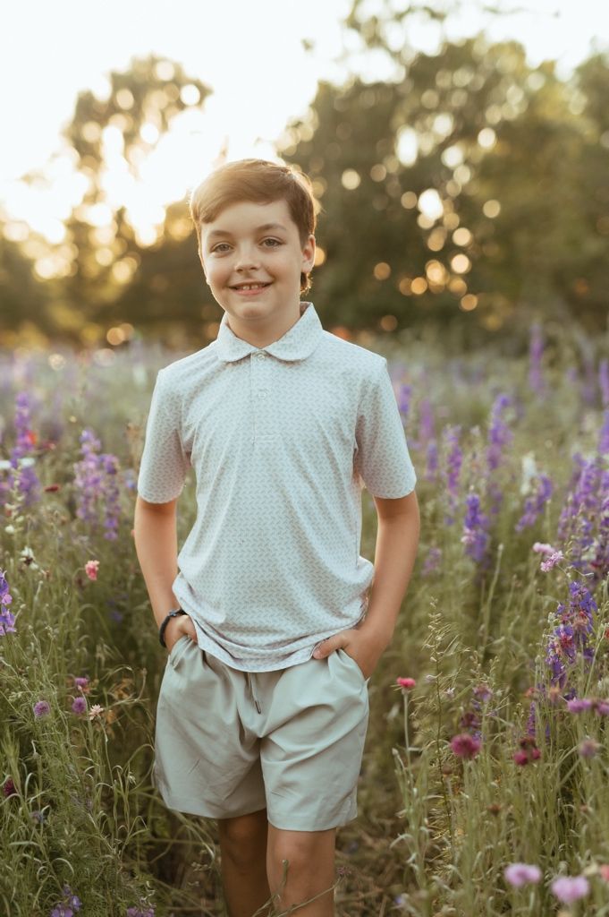 Child in light blue outfit standing among purple wildflowers at sunset in a meadow.