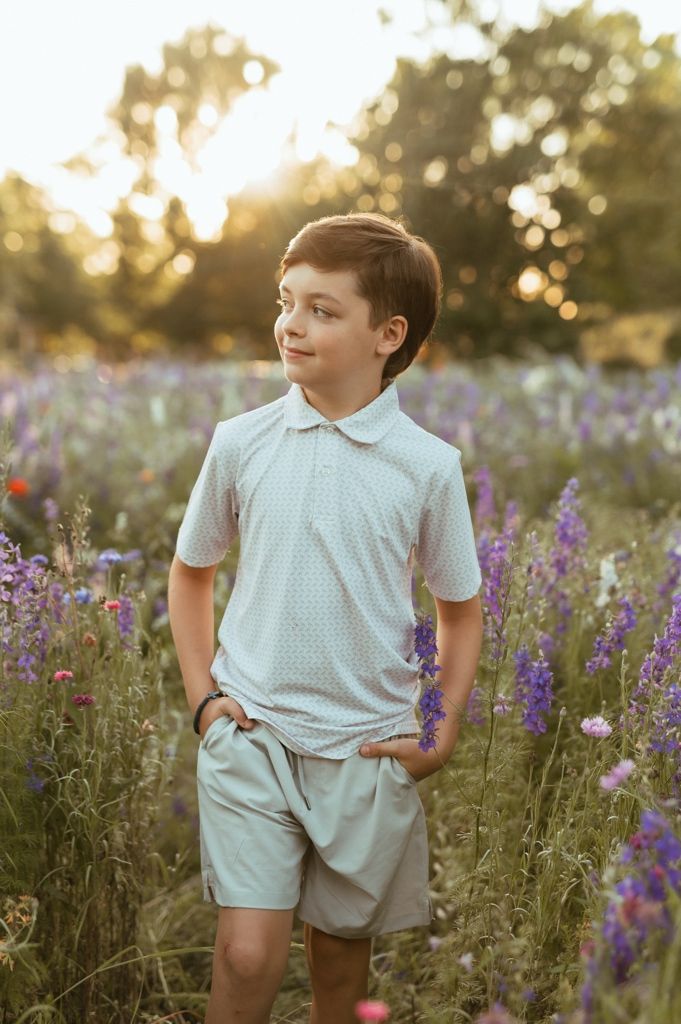 Child wearing light blue outfit stands among vibrant purple wildflowers in golden sunset light.