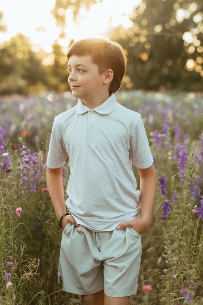 Child in a light blue outfit poses casually among blooming purple wildflowers at sunset.