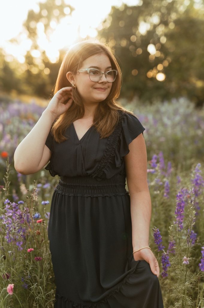 Person in black dress posing amid blooming purple wildflowers during golden hour.