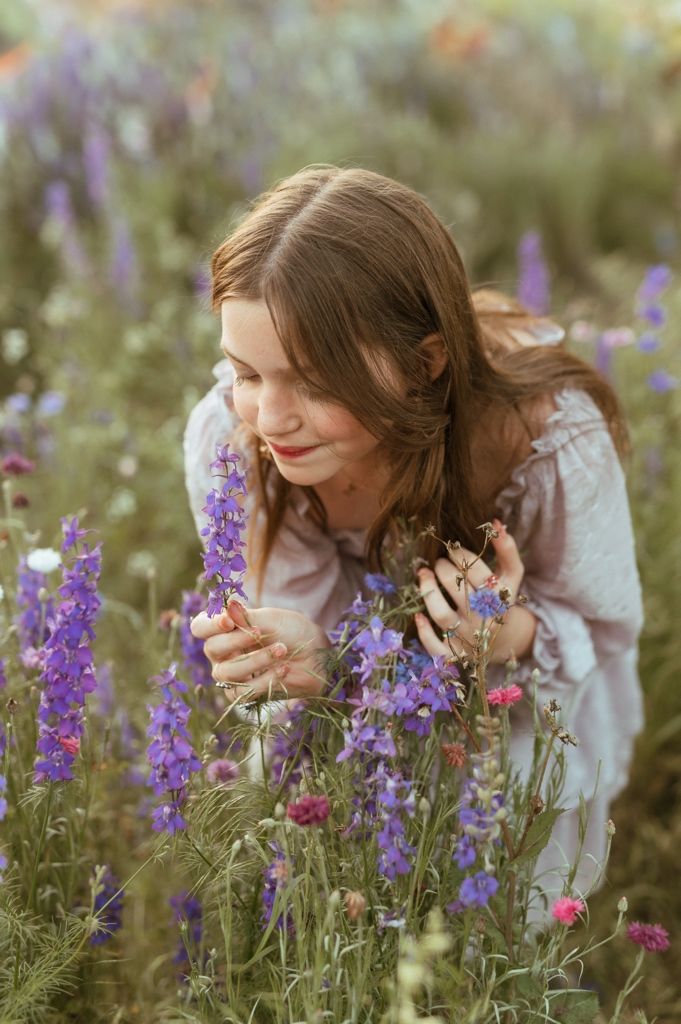 Woman in white dress admiring vibrant purple delphiniums in a summer garden during golden hour.