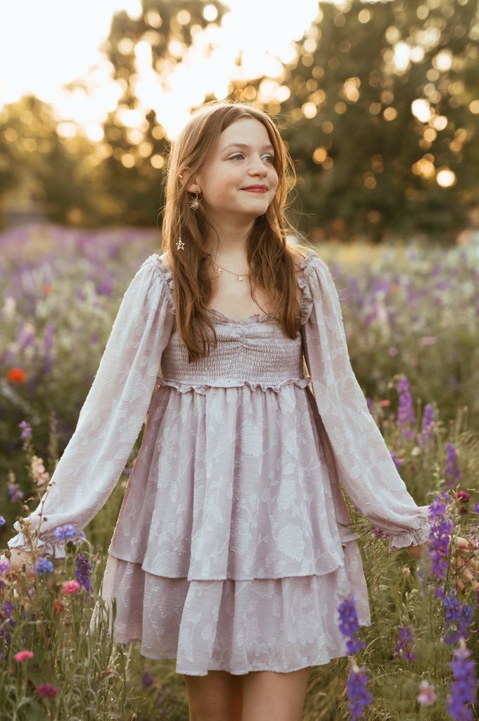 A sunset portrait amidst a meadow of purple flowers wearing a romantic vintage-inspired dress with flowing sleeves.