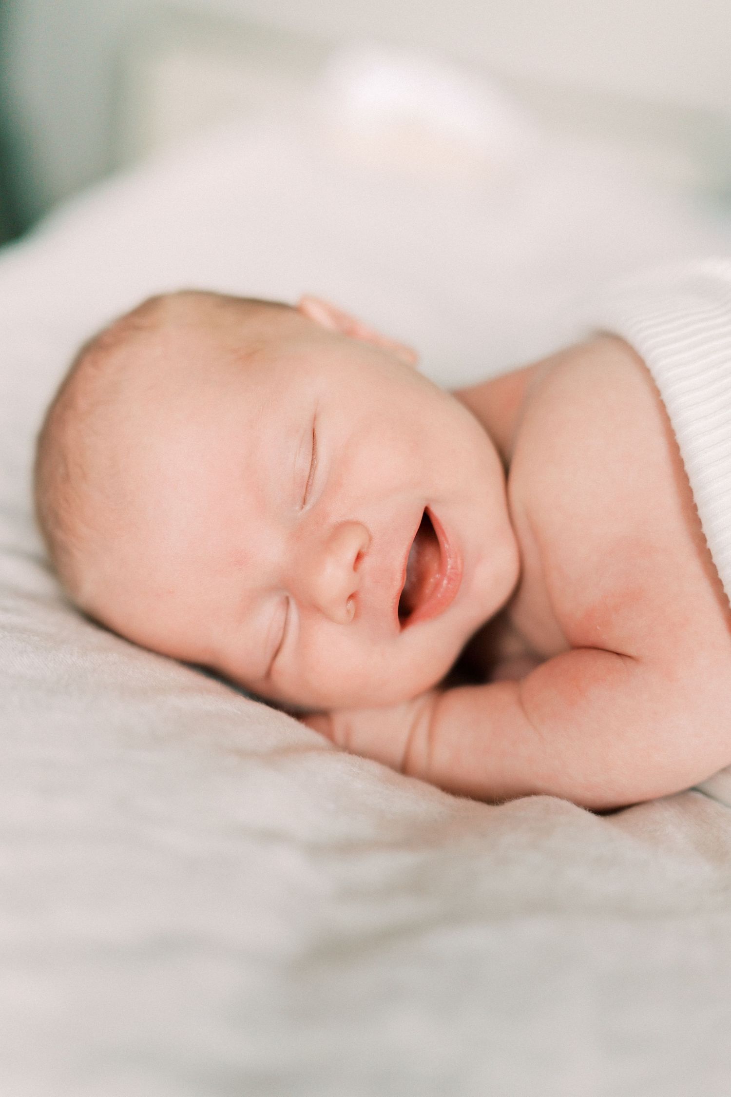 Peaceful sleeping newborn baby lies on soft white bedding, mouth slightly open in gentle slumber.