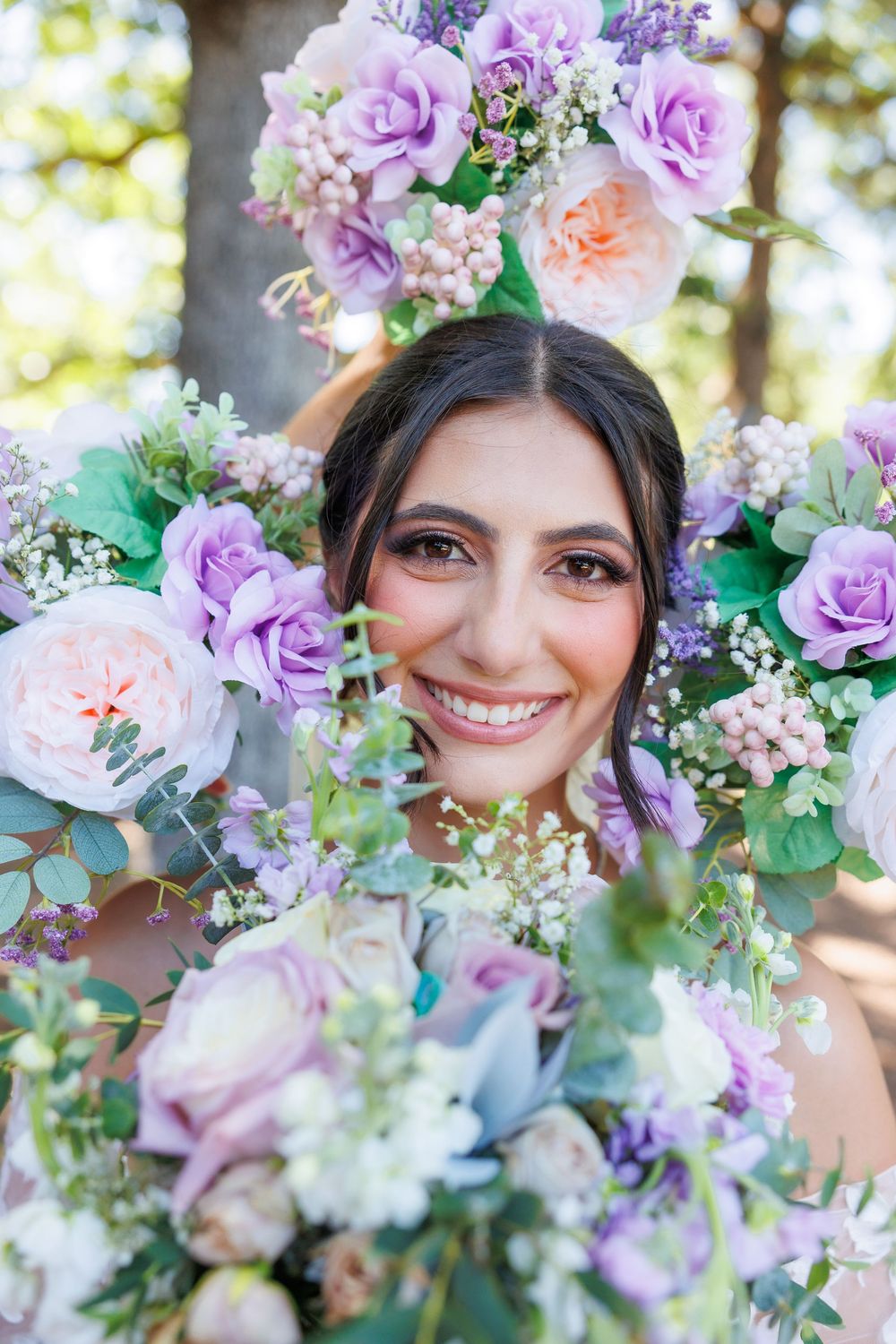 A stunning bridal portrait framed by lavender and pink roses with delicate greenery in natural outdoor lighting.