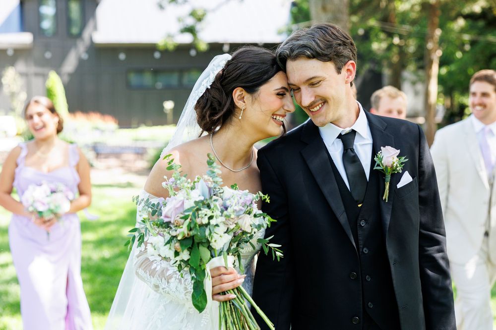 Couple shares an intimate moment outdoors during their wedding celebration with light green foliage in background.