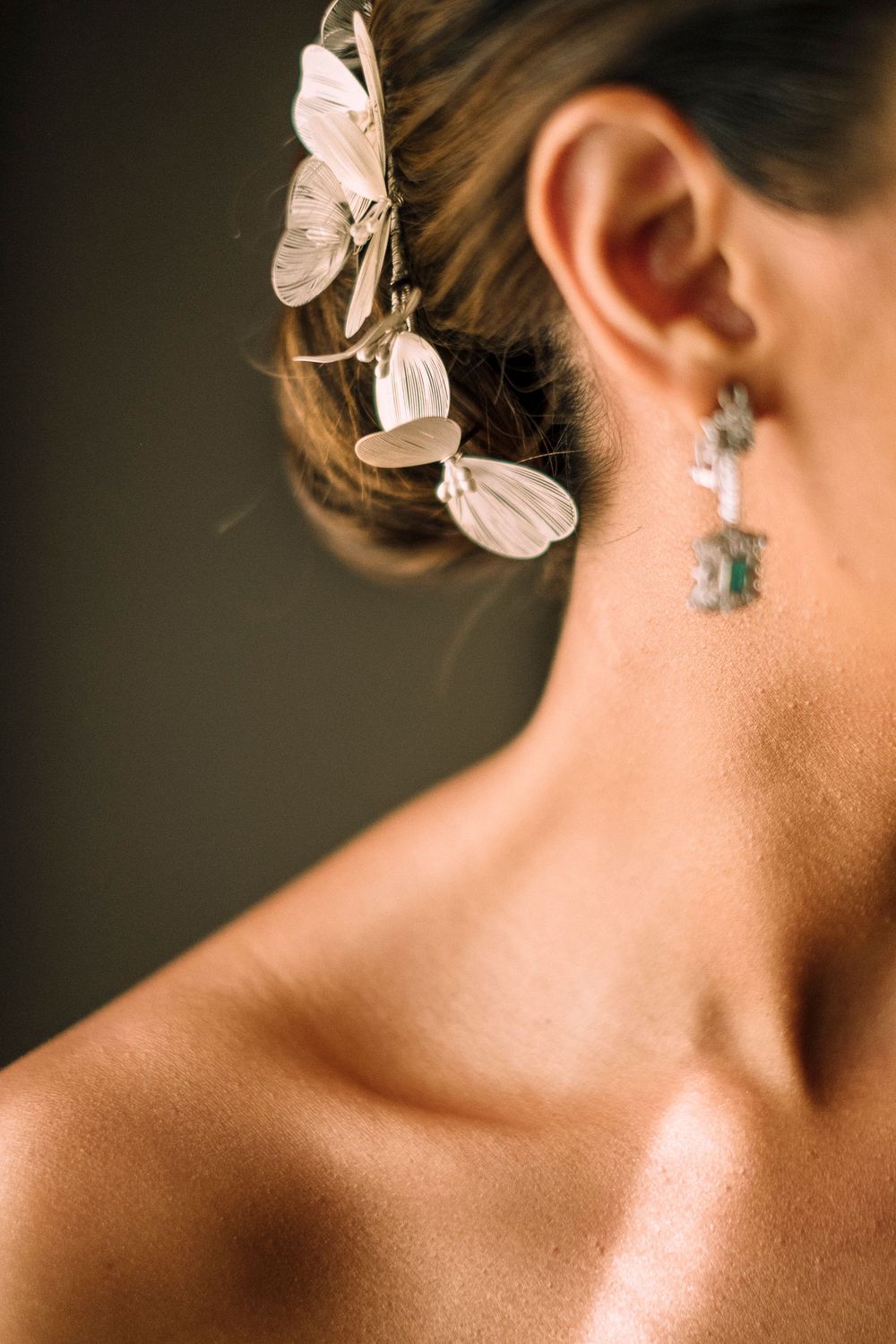 Close-up of delicate butterfly hair accessories and dangling earring with bare shoulder.