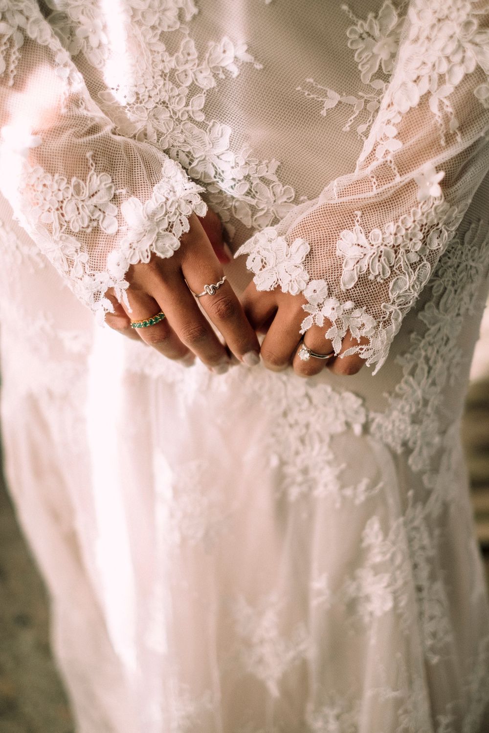 Detail shot of lace wedding dress sleeve with intricate floral patterns and rings on hands.