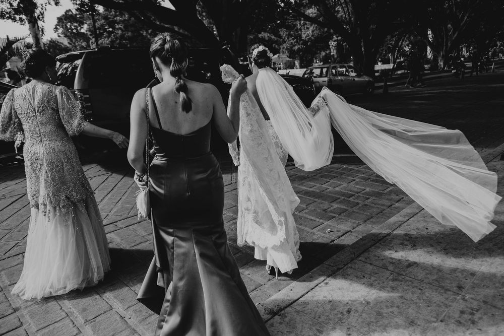 Wedding guests in elegant dresses walk across an outdoor dance floor as a flowing white veil catches the breeze.