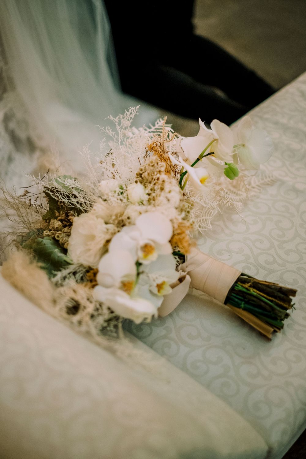 Delicate white bridal bouquet with lace detail and gold accents resting on textured fabric.