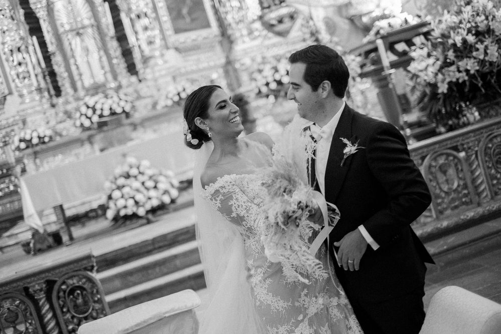 Black and white photograph of newlyweds sharing a joyful moment at church altar.